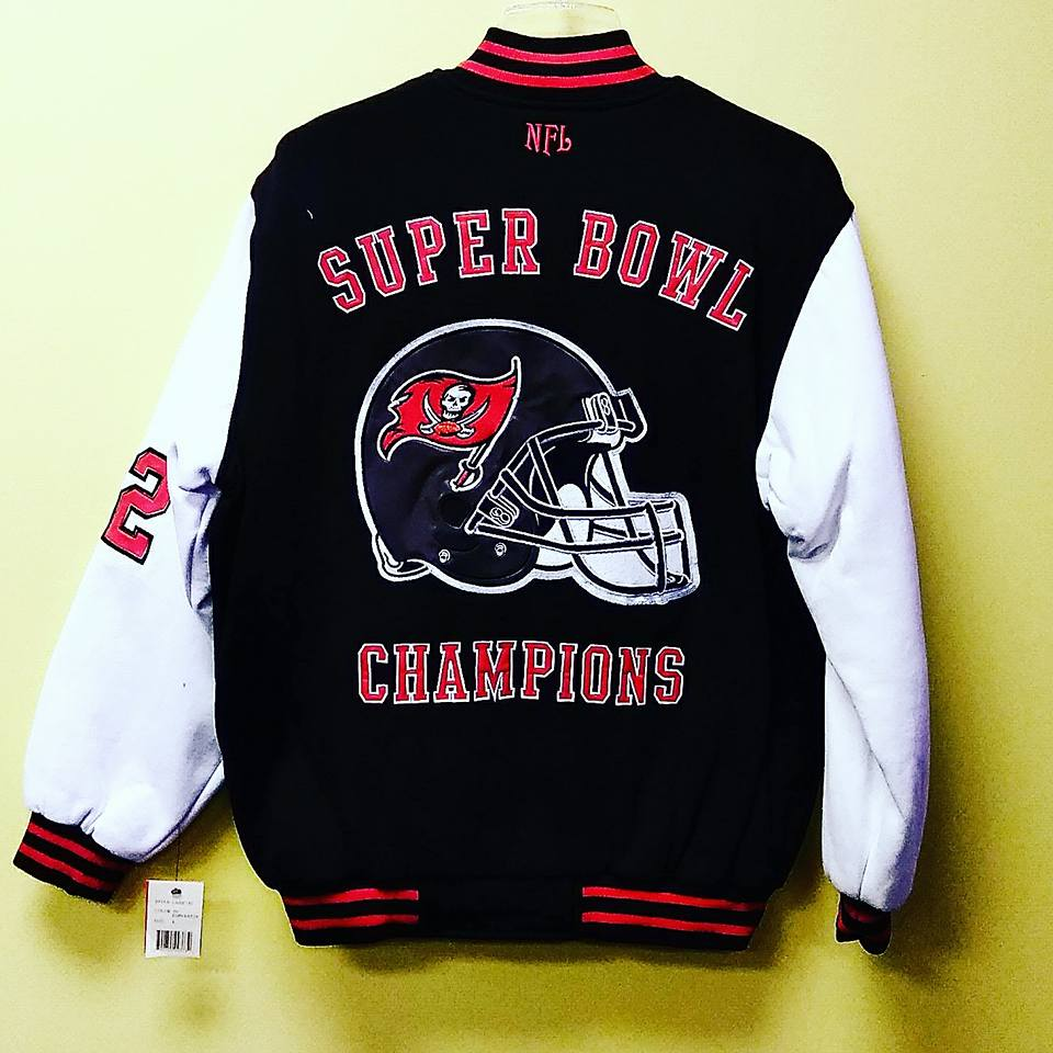A black Tampa Bay Buccaneers Super Bowl Champions varsity jacket with white sleeves and red and black striped trim.
