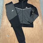 A two-piece Nike tracksuit featuring a black and gray zip-up hooded jacket and matching black and gray sweatpants.