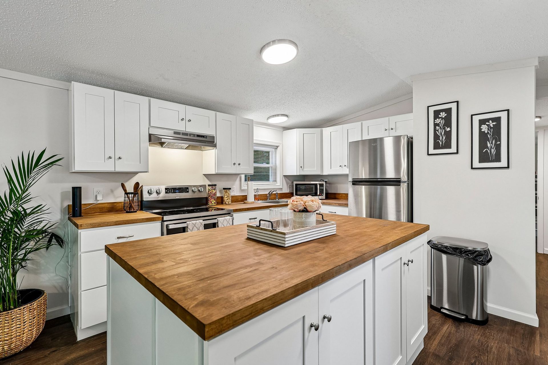 Bright modern kitchen with white cabinets, wood countertops, and stainless steel appliances.