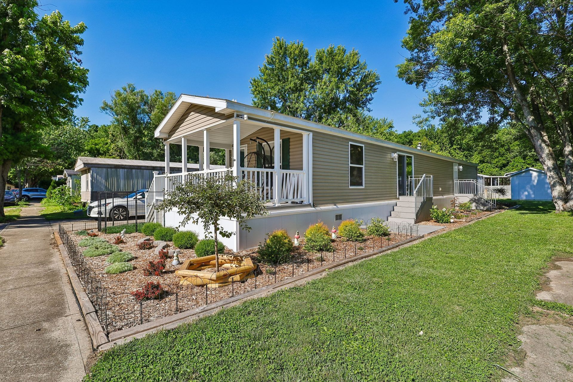 Manufactured home with covered front porch, landscaped yard, and private driveway.