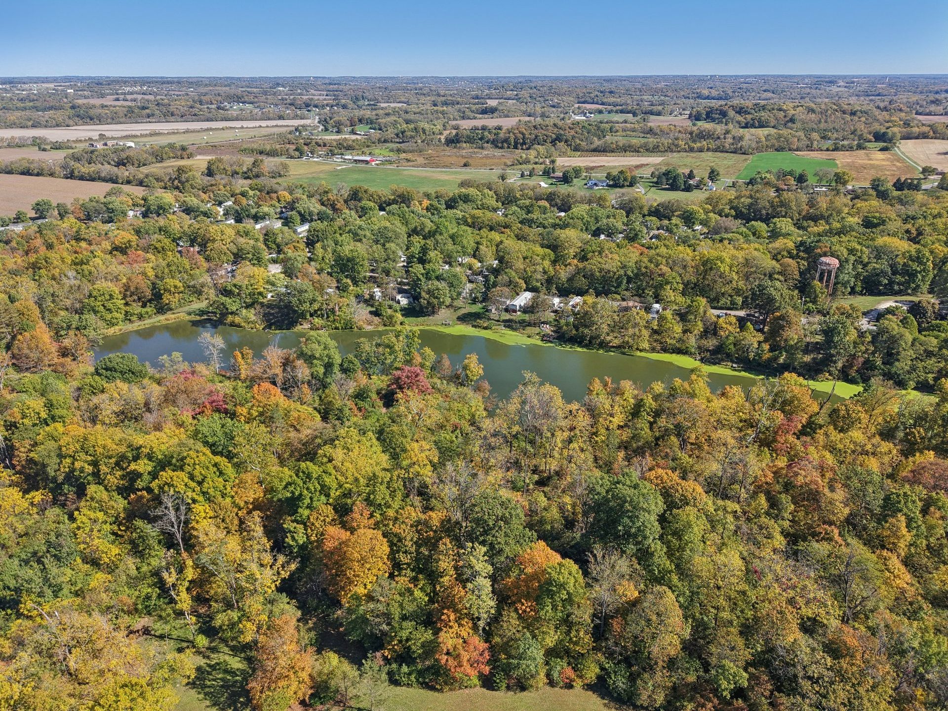 Drone view overlooking wooded community and scenic pond.