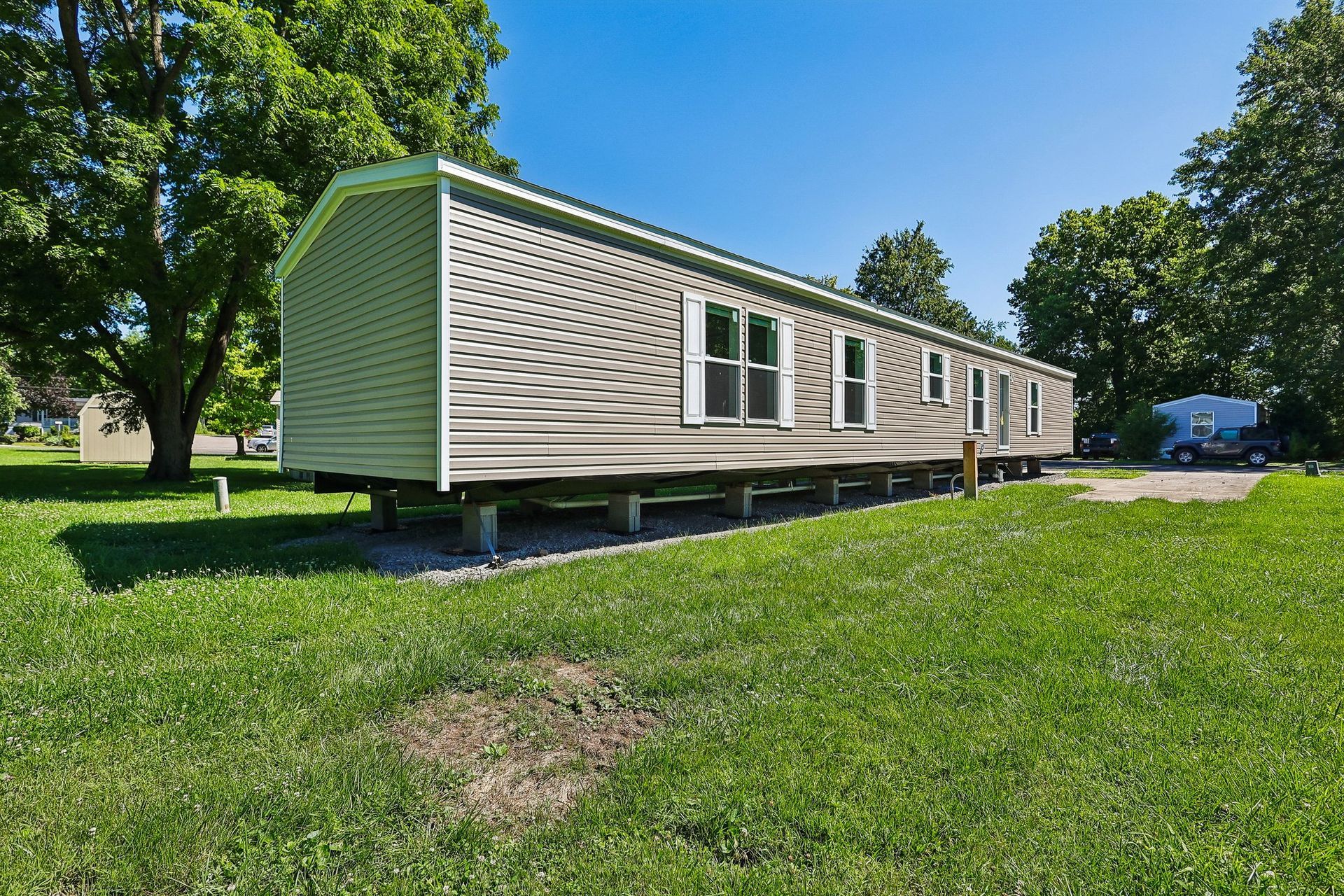 Manufactured home exterior with large yard and mature trees.