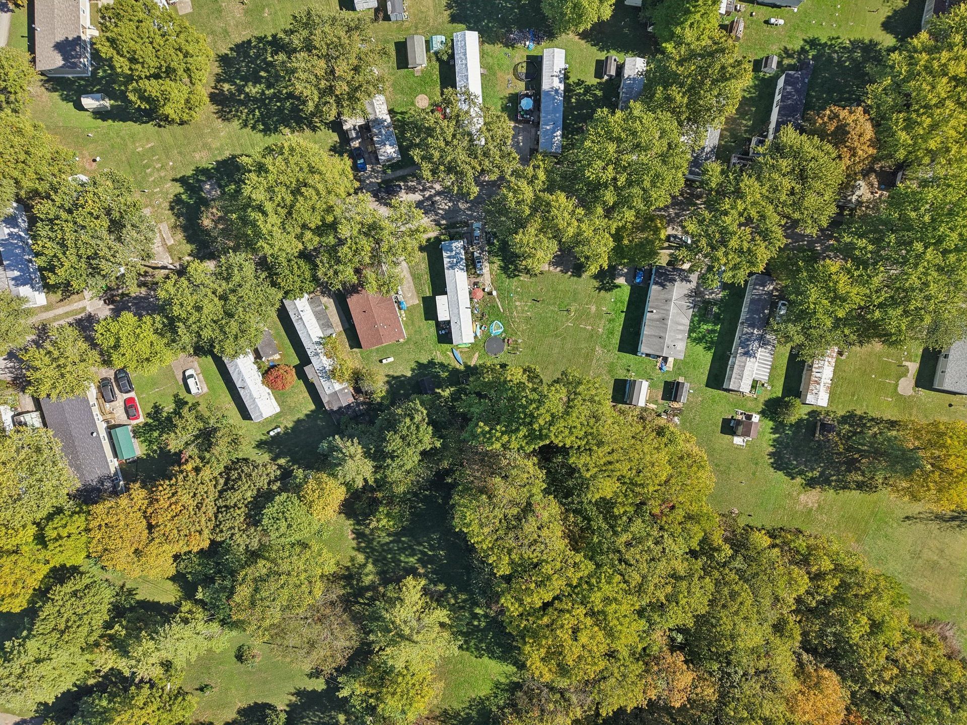 Aerial view of a mobile home park with various trailers and large green trees, on a sunny day.