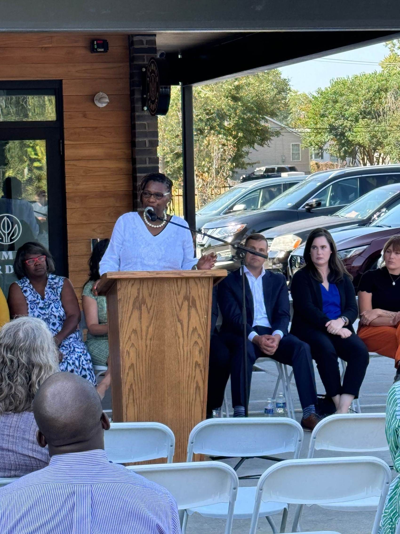 A speaker at the podium under the canopy of the completed Alumnus Gardens building.
