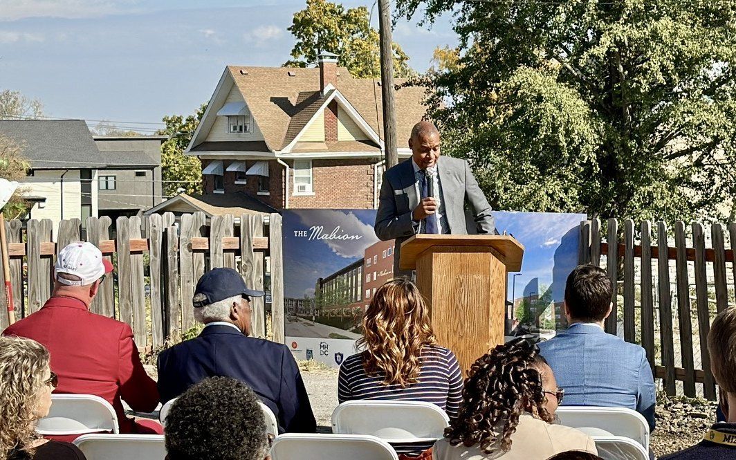 Dr. Troy Nash speaking at The Mabion groundbreaking, the project board beside the podium.