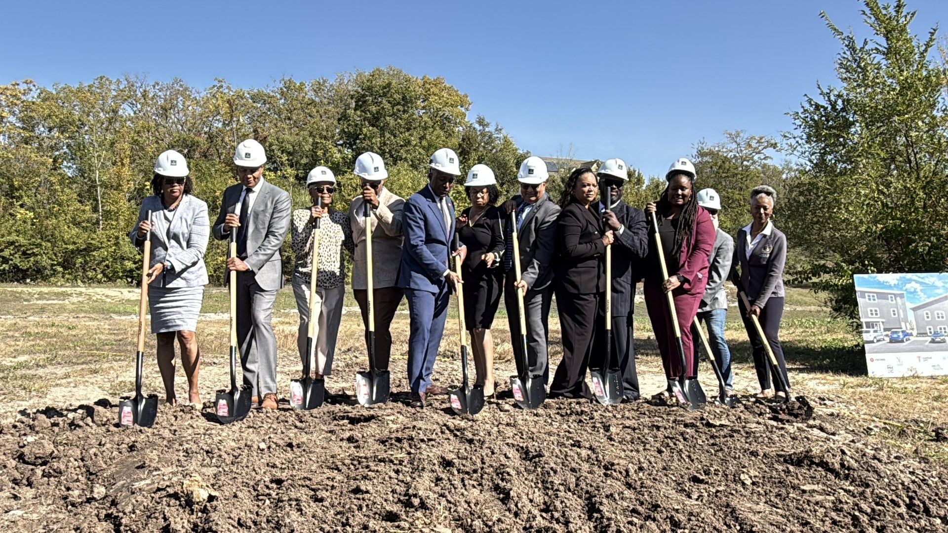 Guests in hard hats holding ceremonial shovels in a line at the Promise Place groundbreaking.