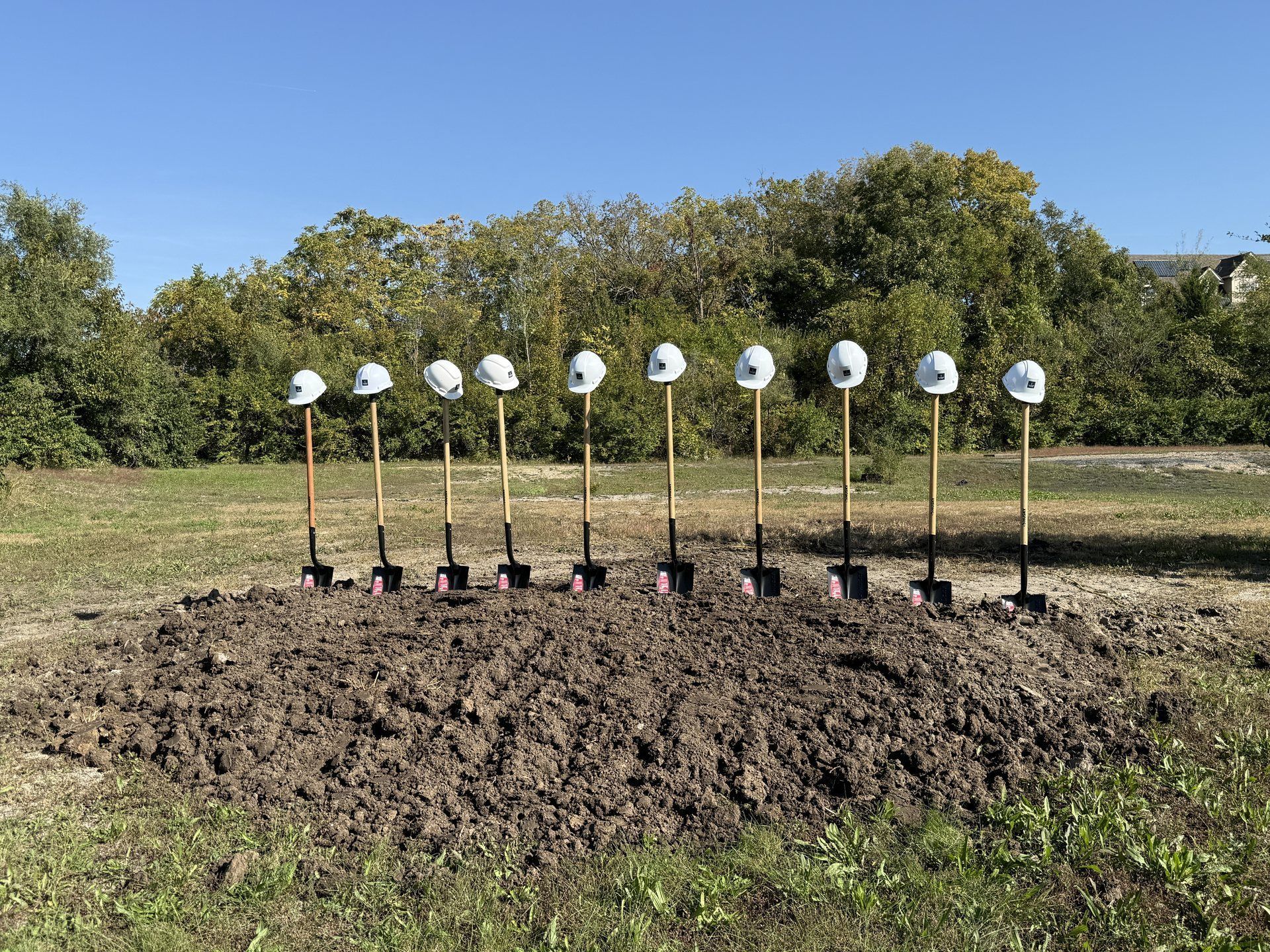 White hard hats on ceremonial shovels lined up in a mound of earth at the Promise Place site.