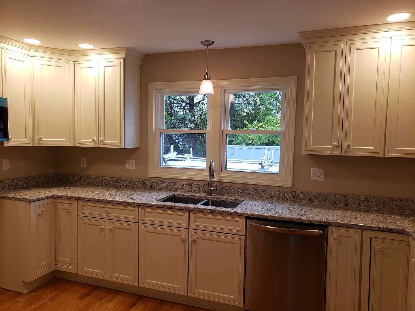 A kitchen with white cabinets , granite counter tops , a sink and a window.