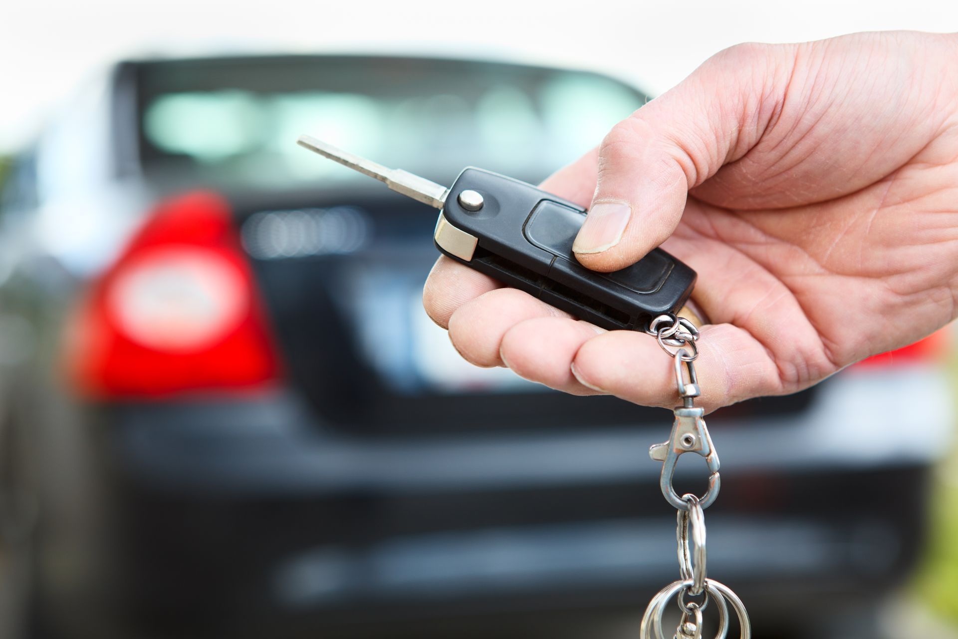 Mano che tiene le chiavi dell'auto con un portachiavi nero, un'auto sullo sfondo sfocato.