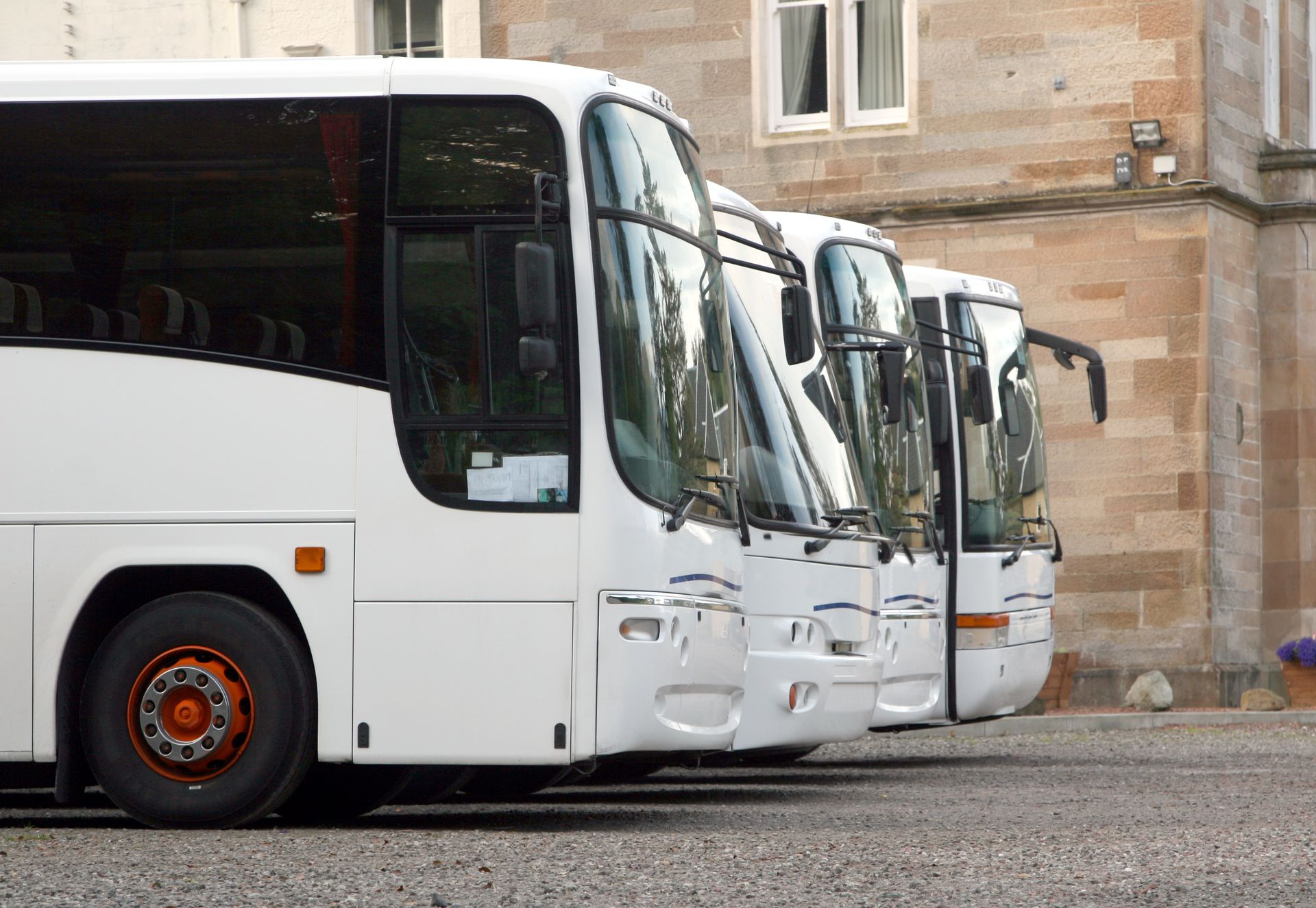 Autobus turistici bianchi parcheggiati in fila davanti a un edificio in pietra.