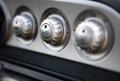 Primo piano del pannello di controllo del clima dell'auto con tre quadranti argentati, tra cui i comandi dell'aria condizionata e della temperatura.