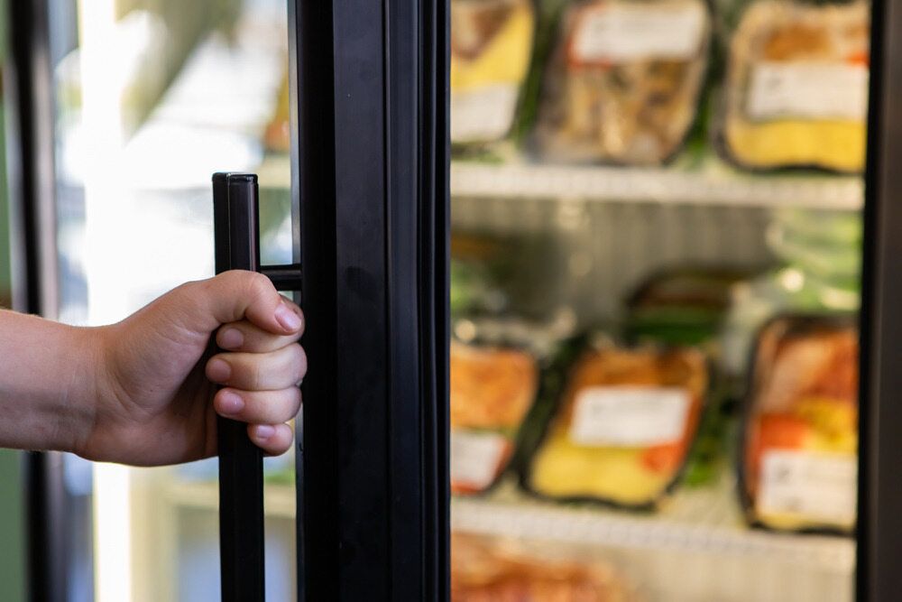 A Person is Opening a Refrigerator Door in a Grocery Store — Noosa Refrigeration & Air-conditioning in Cooroy, QLD