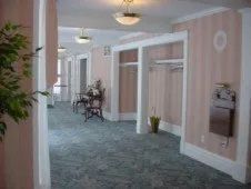 Hallway with pink walls, green carpet, and open doorways. A plant and furniture are visible.