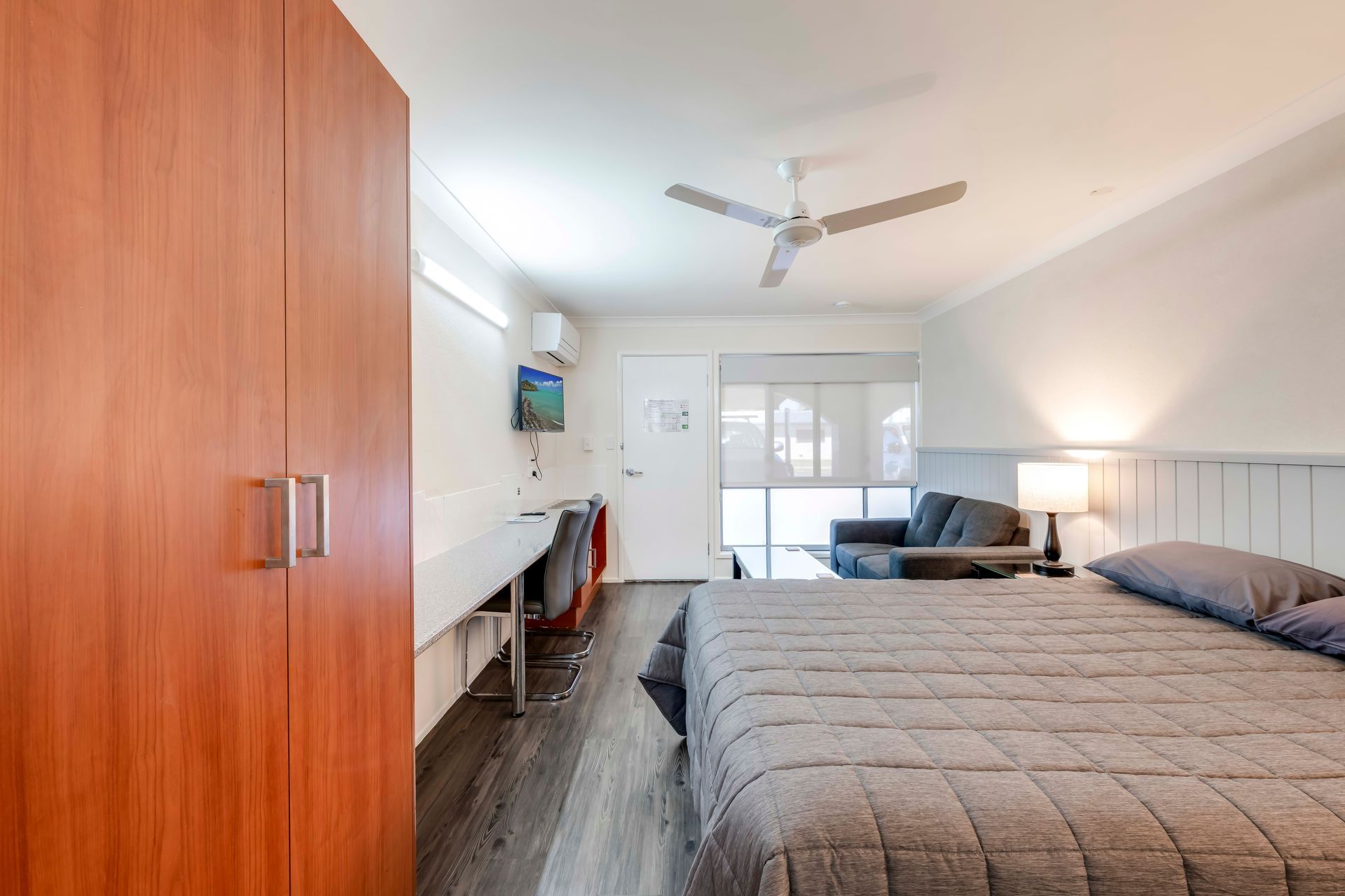 Bright bedroom with twin beds, desk, chairs, and blue accents in a compact hotel-style room.