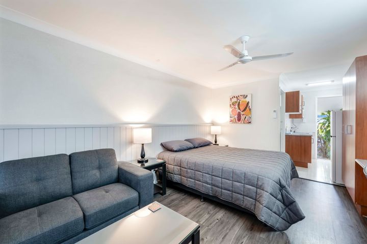 Bright bedroom with twin beds, desk, chairs, and blue accents in a compact hotel-style room.