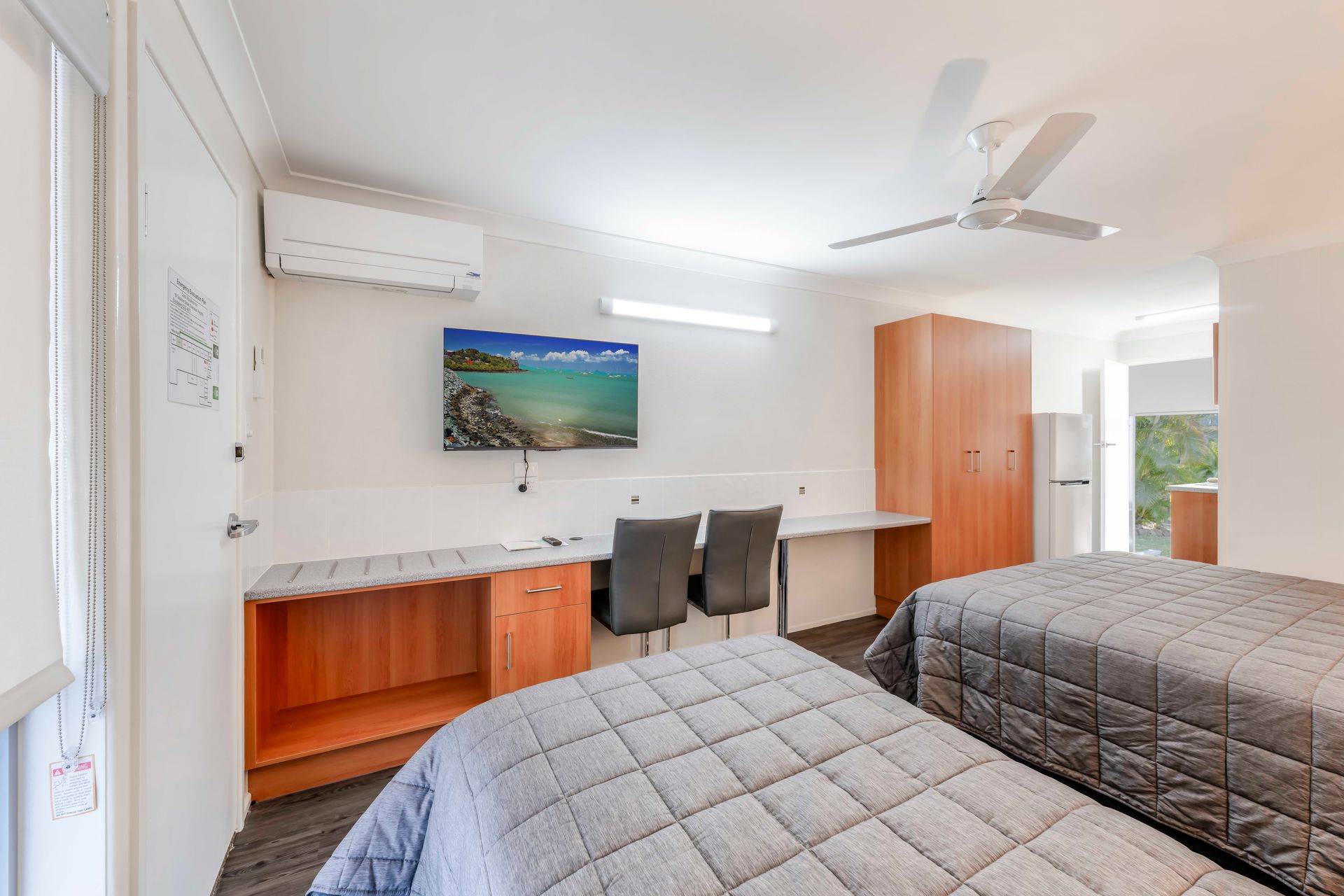 Bright bedroom with two beds, white walls, ceiling fan, and landscape artwork.