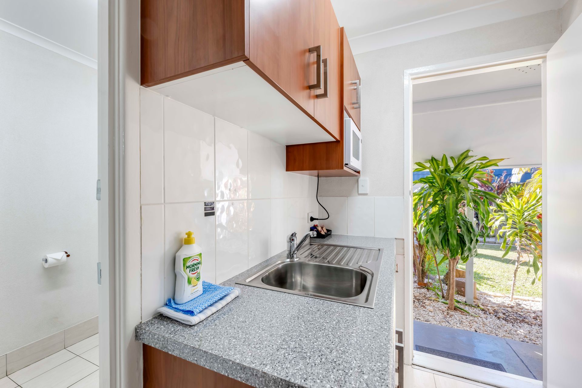 Compact kitchen corner with white shelves, a microwave, and a gray countertop beside a cabinet.