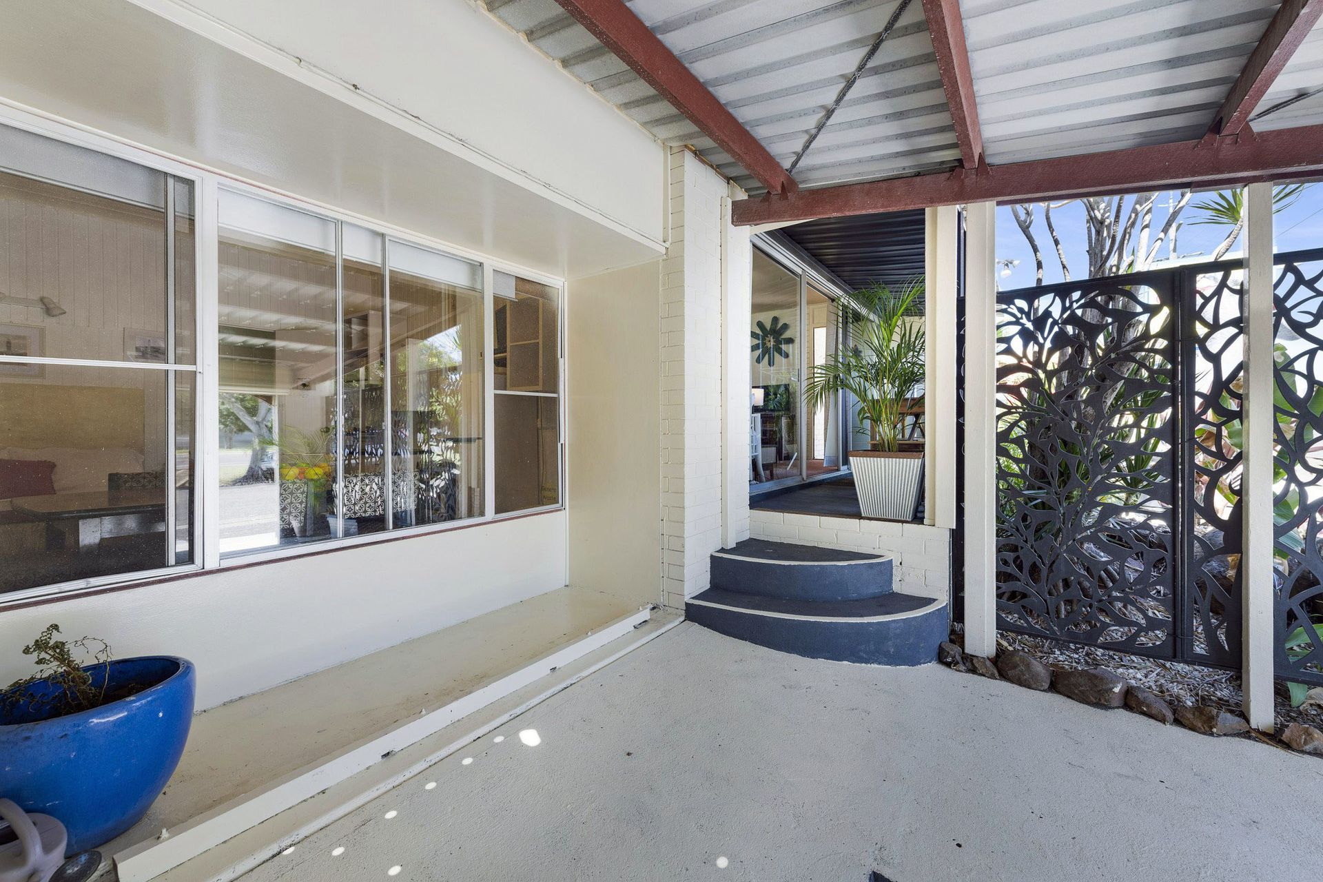 Covered front porch with steps, windows, and a blue planter beside a decorative screen fence.