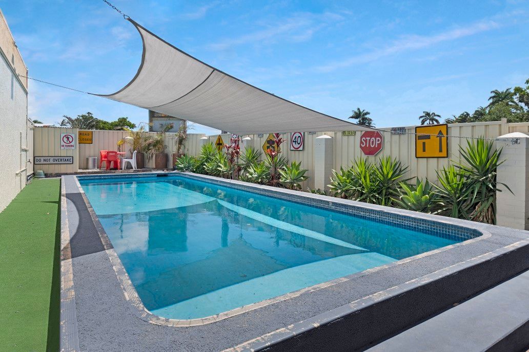 Modern outdoor swimming pool with blue water, white shade sails, and tropical plants beside a concrete deck