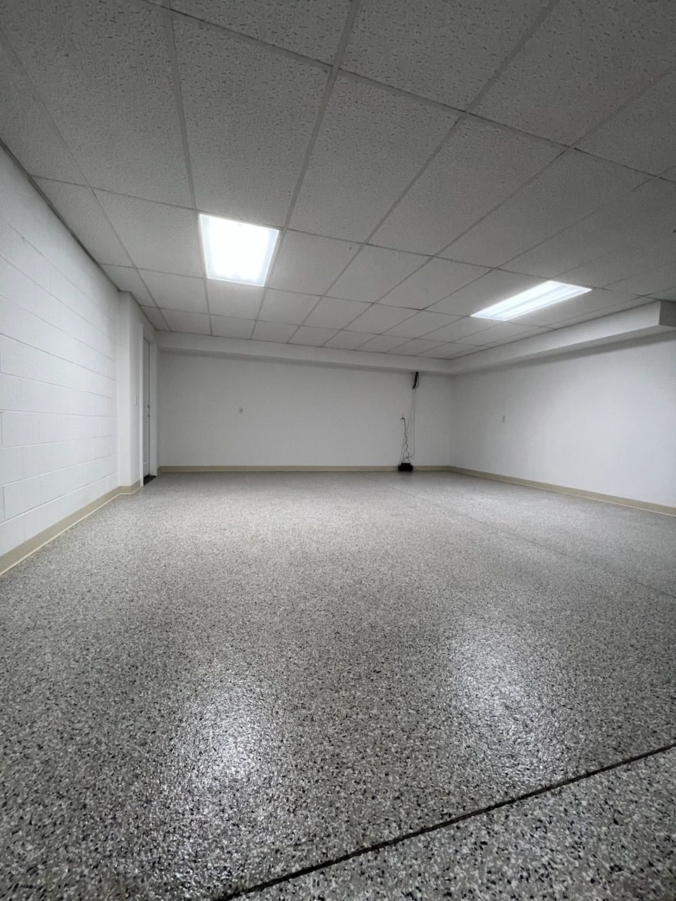 Empty white room with speckled gray floor and fluorescent ceiling lights