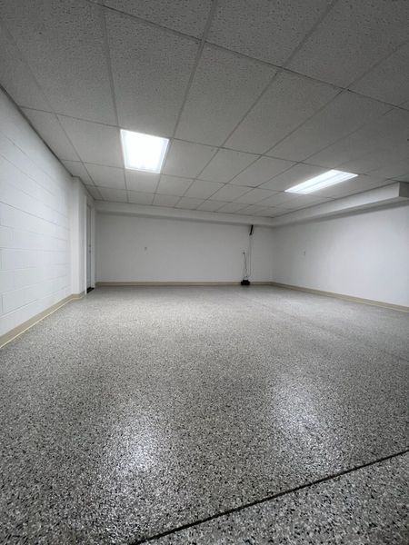Empty white room with speckled gray floor and fluorescent ceiling lights