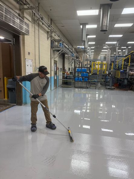Worker using a long-handled mop on a glossy factory floor in a large industrial facility