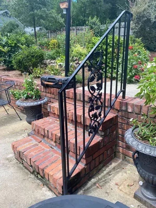 Brick outdoor steps with black wrought-iron railing in a garden patio area