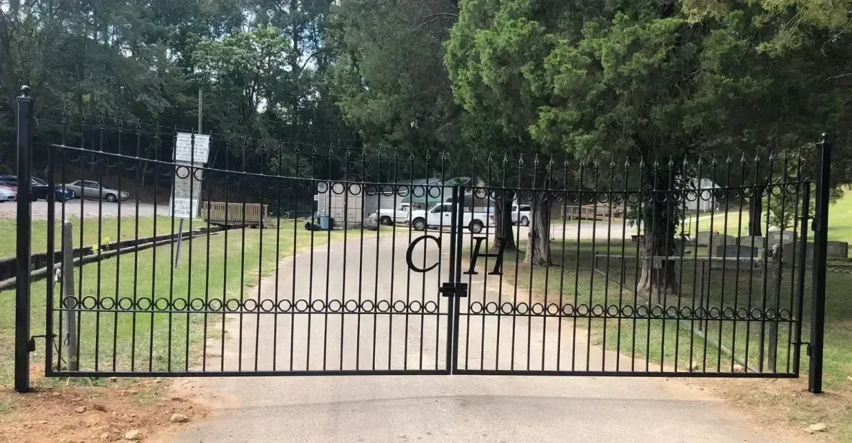 Black metal gate across a gravel path in a tree-lined park or garden entrance.