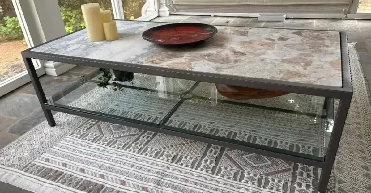 Outdoor patio coffee table with stone top, black metal frame, tray, candles, and decorative glass beneath