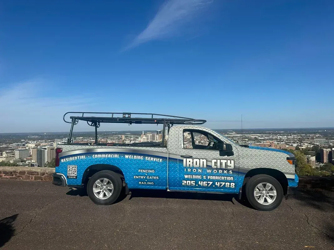Blue Iron City roof-rack pickup truck parked on a hill overlooking a city skyline