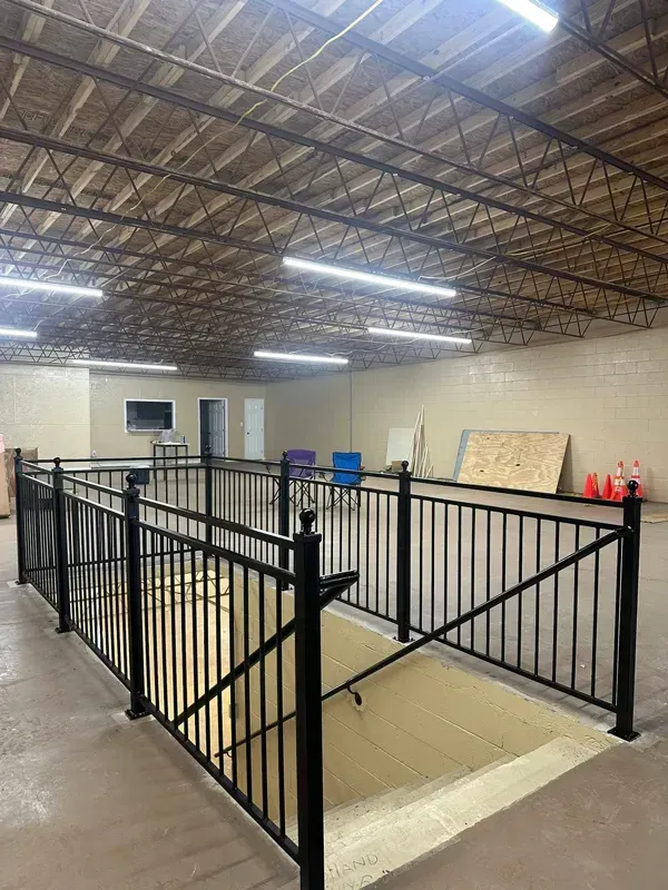 Indoor warehouse-like room with black metal railings around a recessed floor area and fluorescent lights above