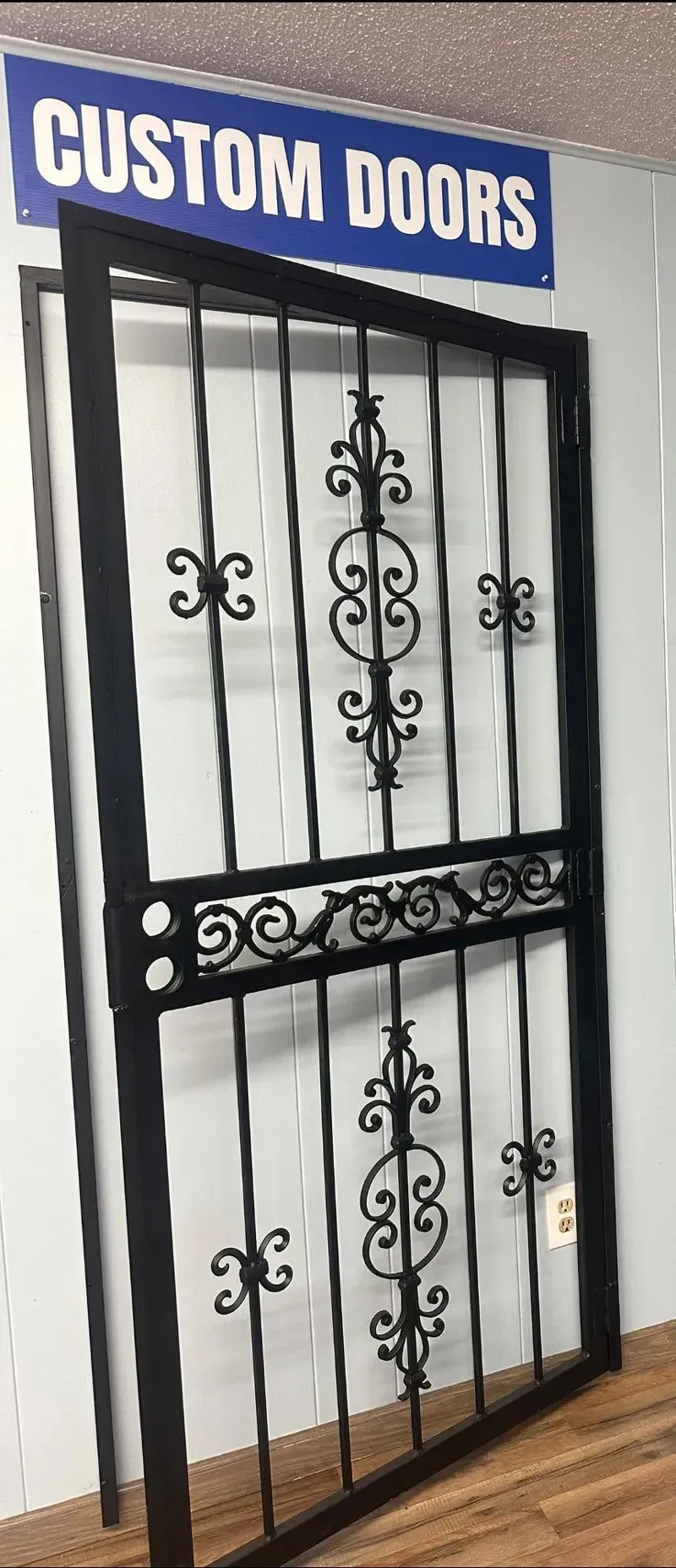 Custom black wrought-iron door with decorative scrollwork and a “CUSTOM DOORS” sign above it
