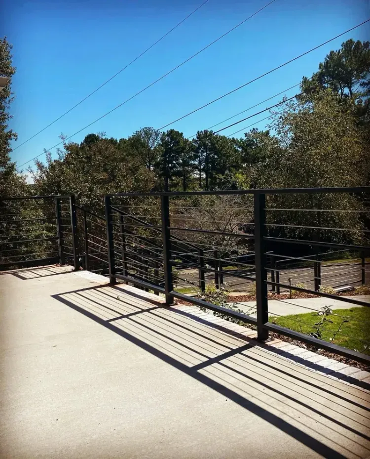 Black metal railing on a sunlit walkway beside trees and power lines under a clear blue sky.