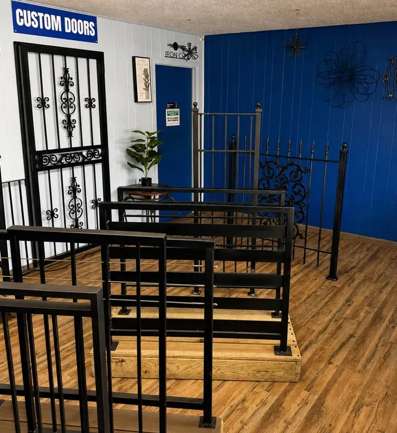 Custom doors and decorative black metal gate displays in a showroom with blue walls and wood floor