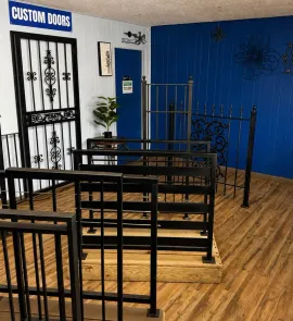 Metal security doors and gates displayed in a showroom with blue walls and wood flooring
