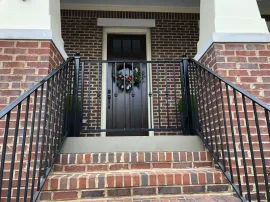 Front porch with brick steps, black metal railings, and a dark front door with a wreath