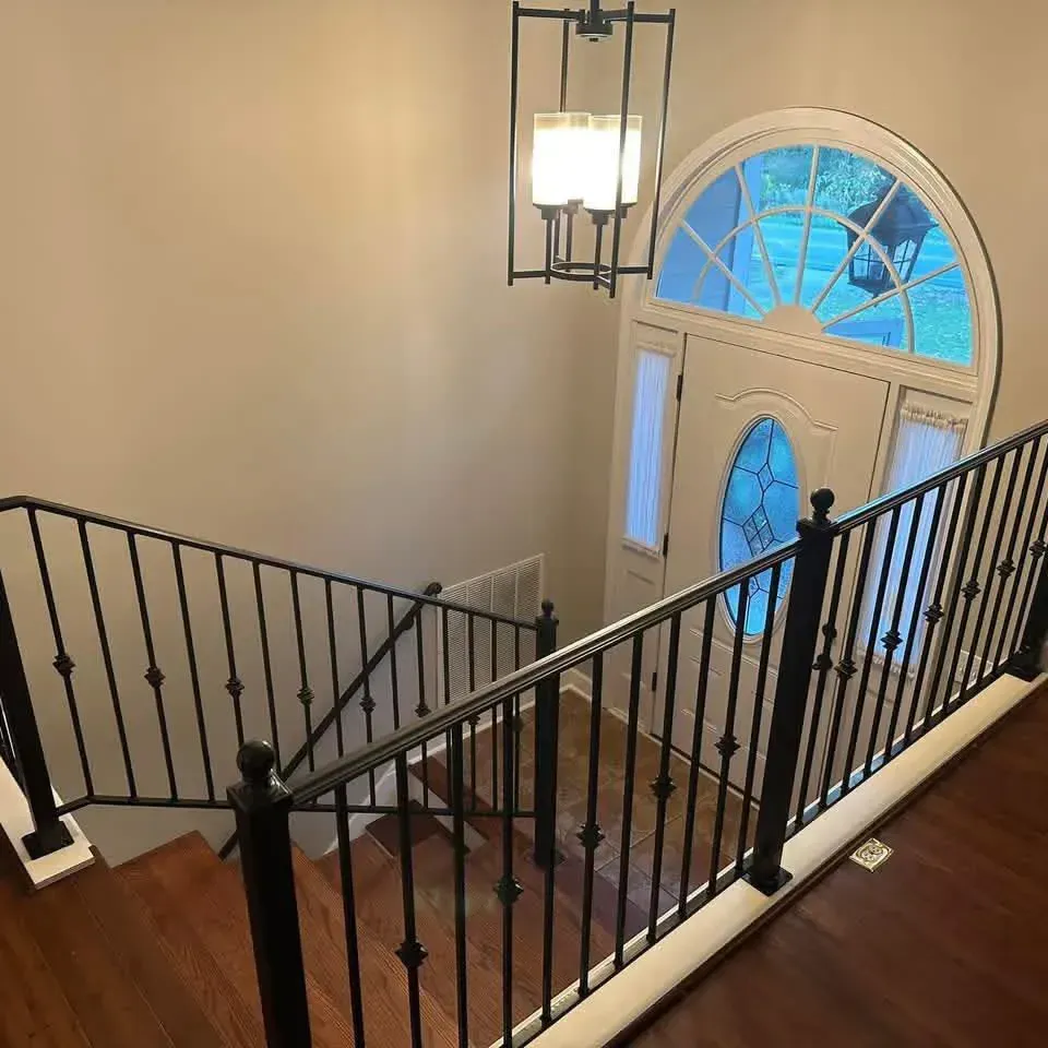 Stairwell with black railings, wooden floors, and a bright front door with an arched window.
