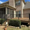 Brick house with a screened porch and black railing over a small yard.