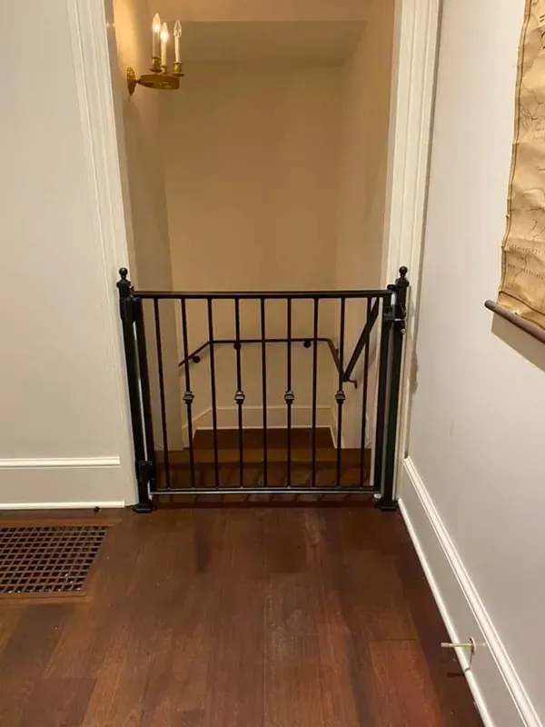 Black safety gate blocking a hallway doorway with a candle sconce and wooden floor