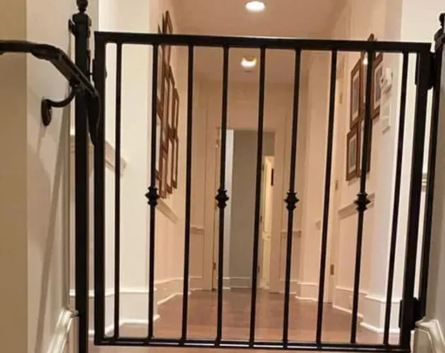 Black metal safety gate blocking a hallway stair landing with beige walls and framed pictures