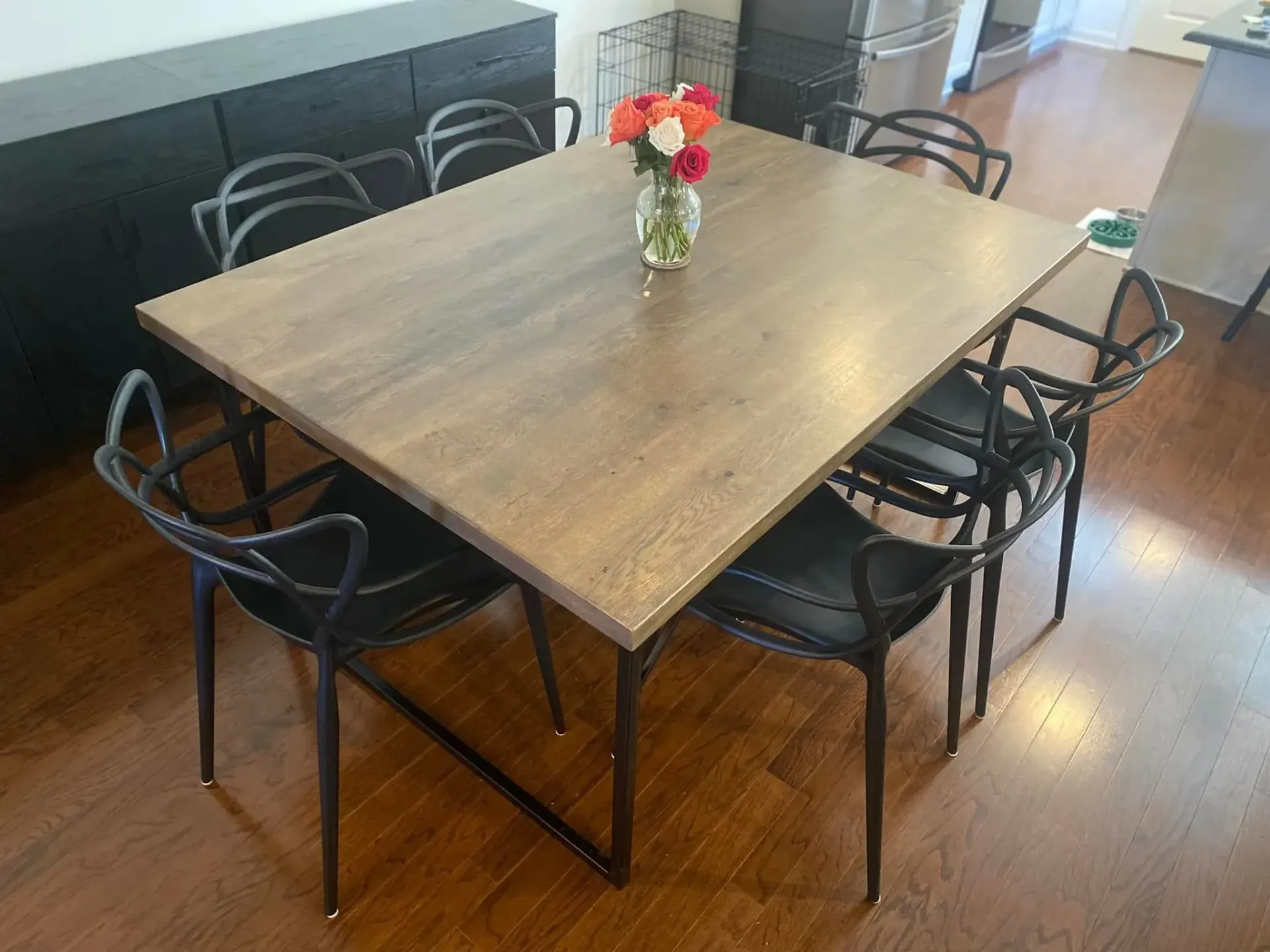 Wooden dining table with black chairs and a small flower vase in a bright room