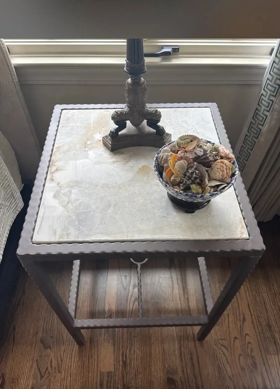 Small wooden side table by a window with a lamp and a decorative bowl of ornaments.