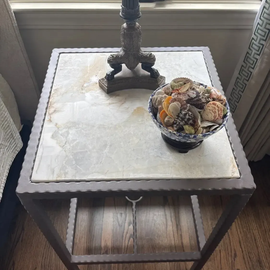 Small side table by a window with a lamp base and a bowl of decorative balls on top.