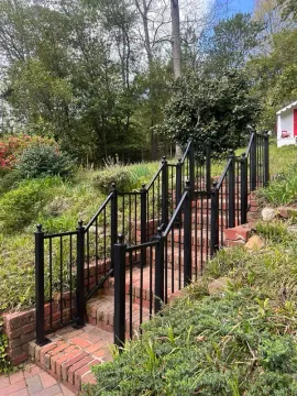 Brick stairway with black metal railings leading up a grassy slope beside a house