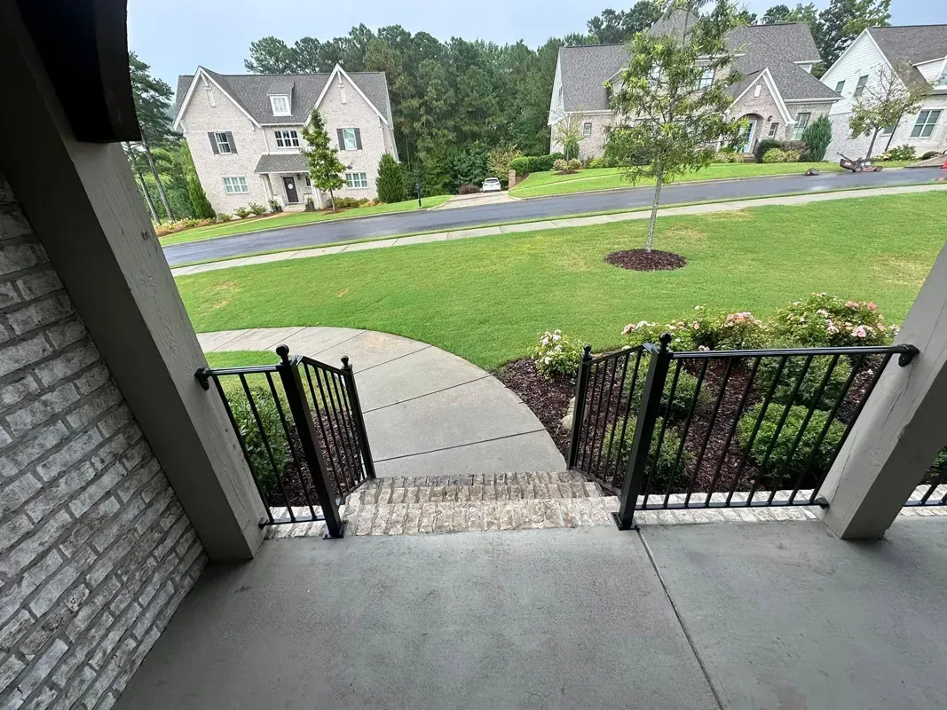 View from a porch steps to a sidewalk, green lawn, and suburban homes across the street.