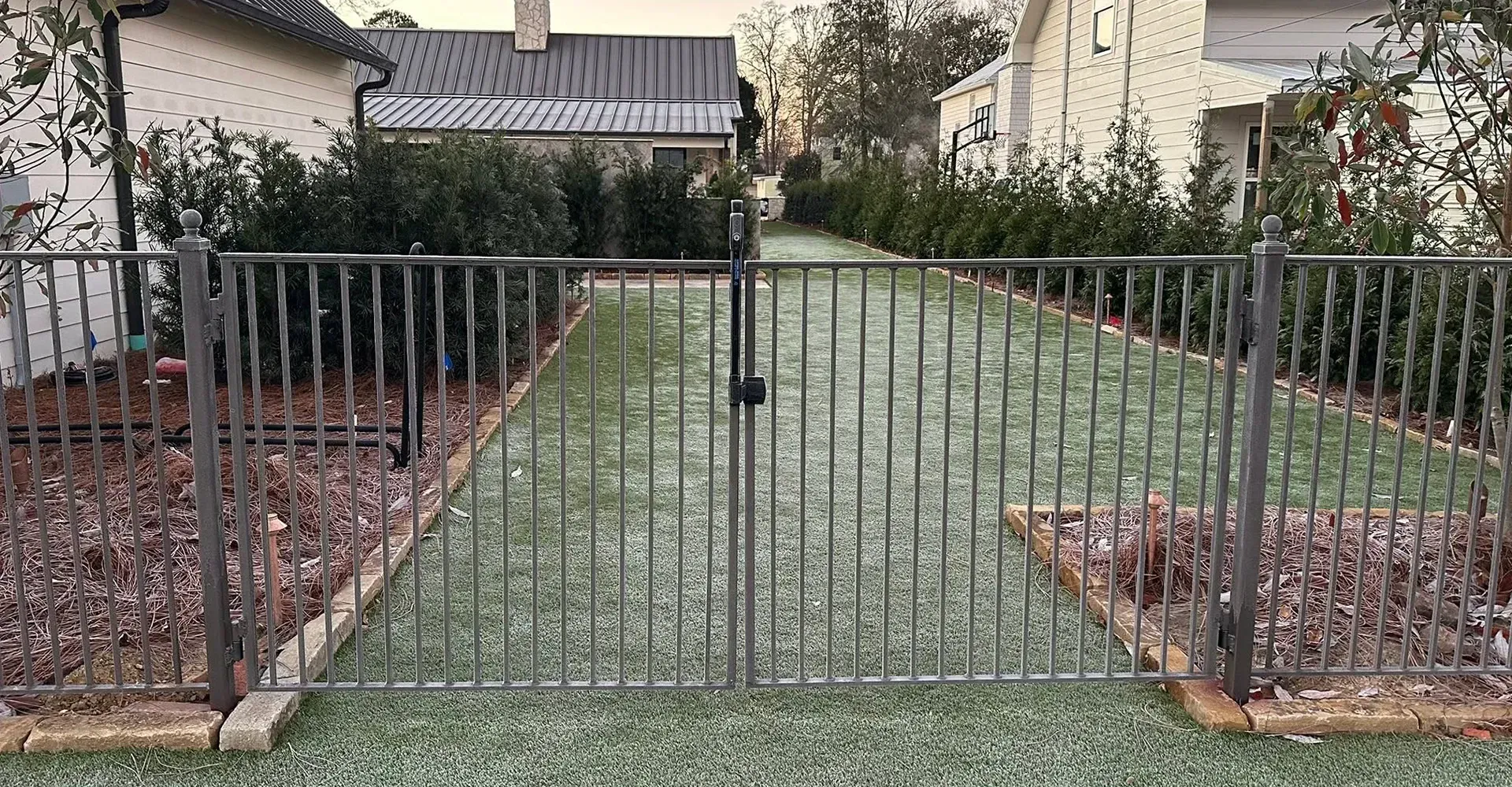 Closed metal gate leading to a front yard path between landscaped beds and houses