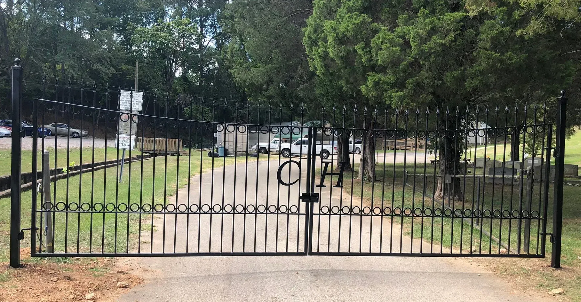 Black metal gate across a gravel path in a tree-lined park or garden entrance.