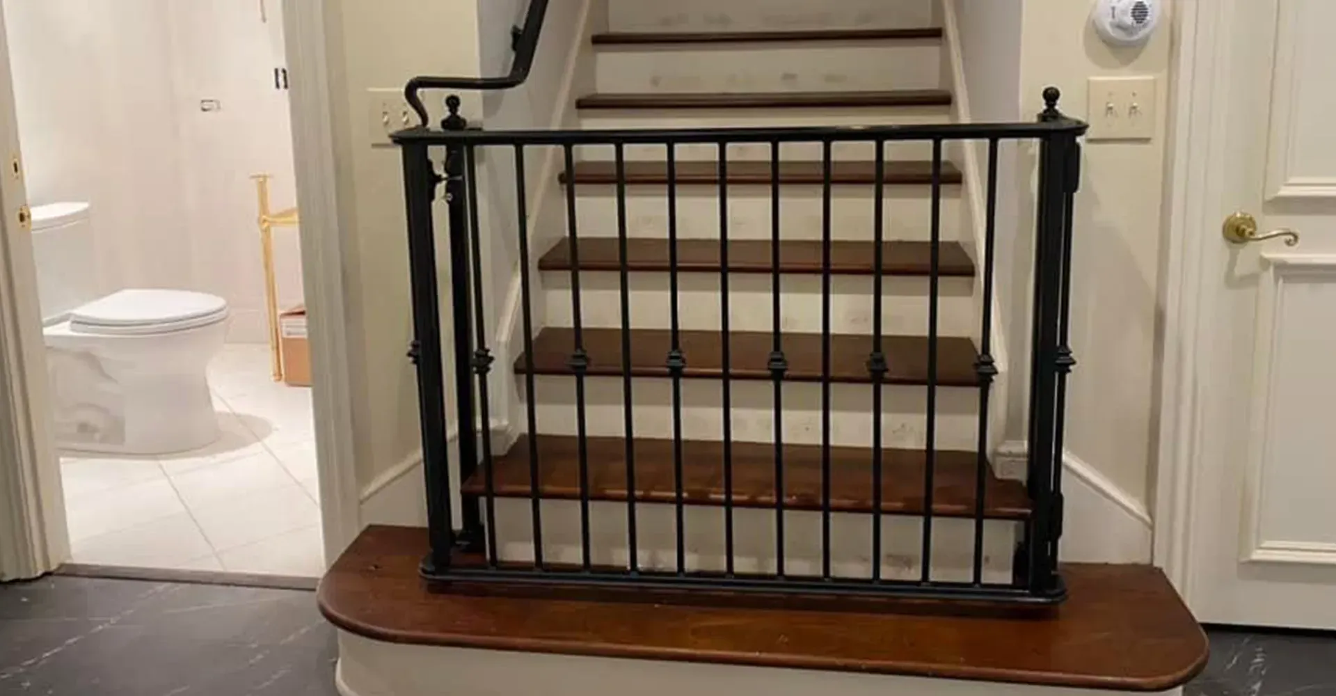 Black metal safety gate at bottom of carpeted staircase in a cream-colored hallway