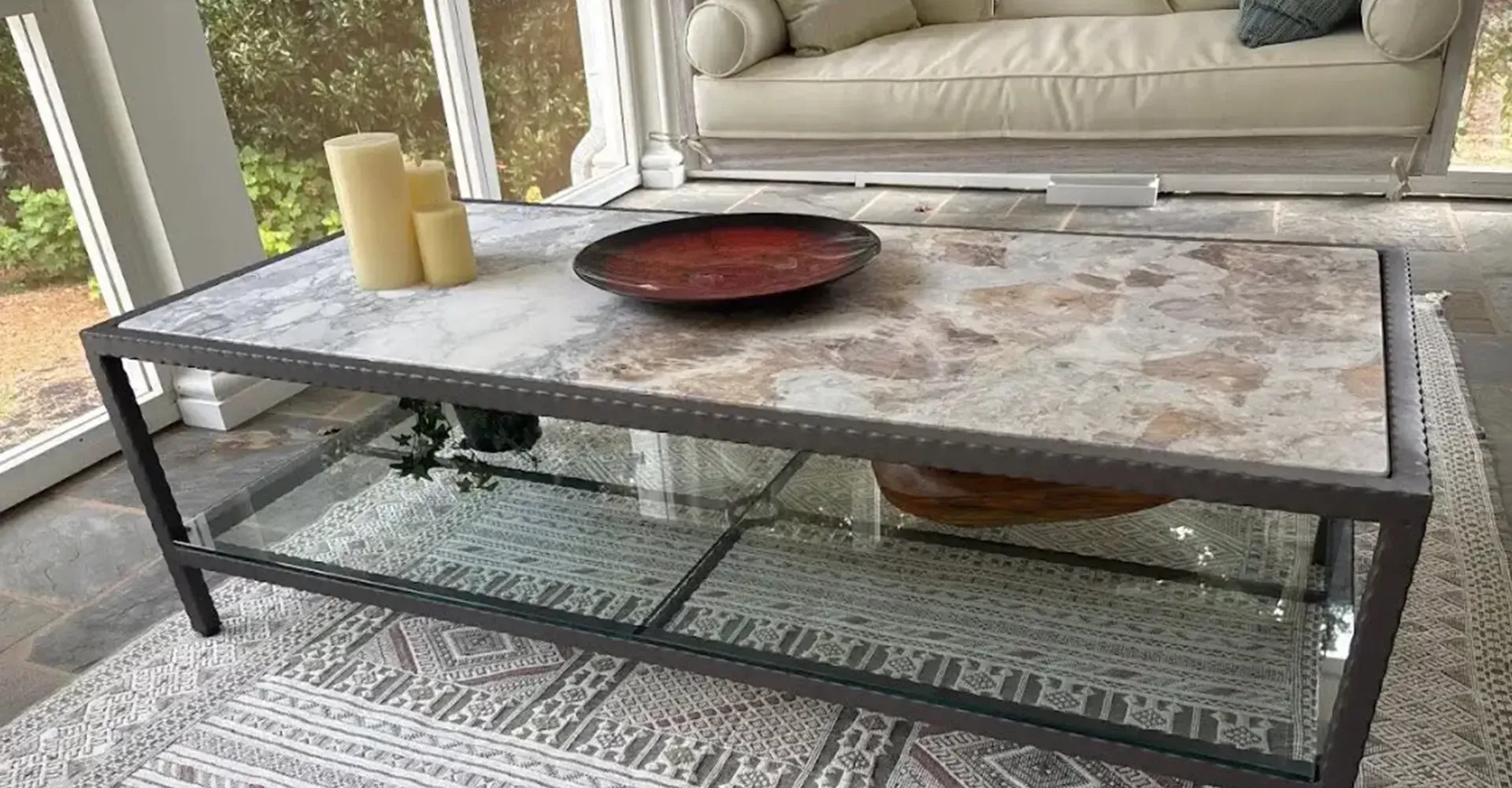 Marble coffee table with candles and bowl on a patterned rug in a bright living room