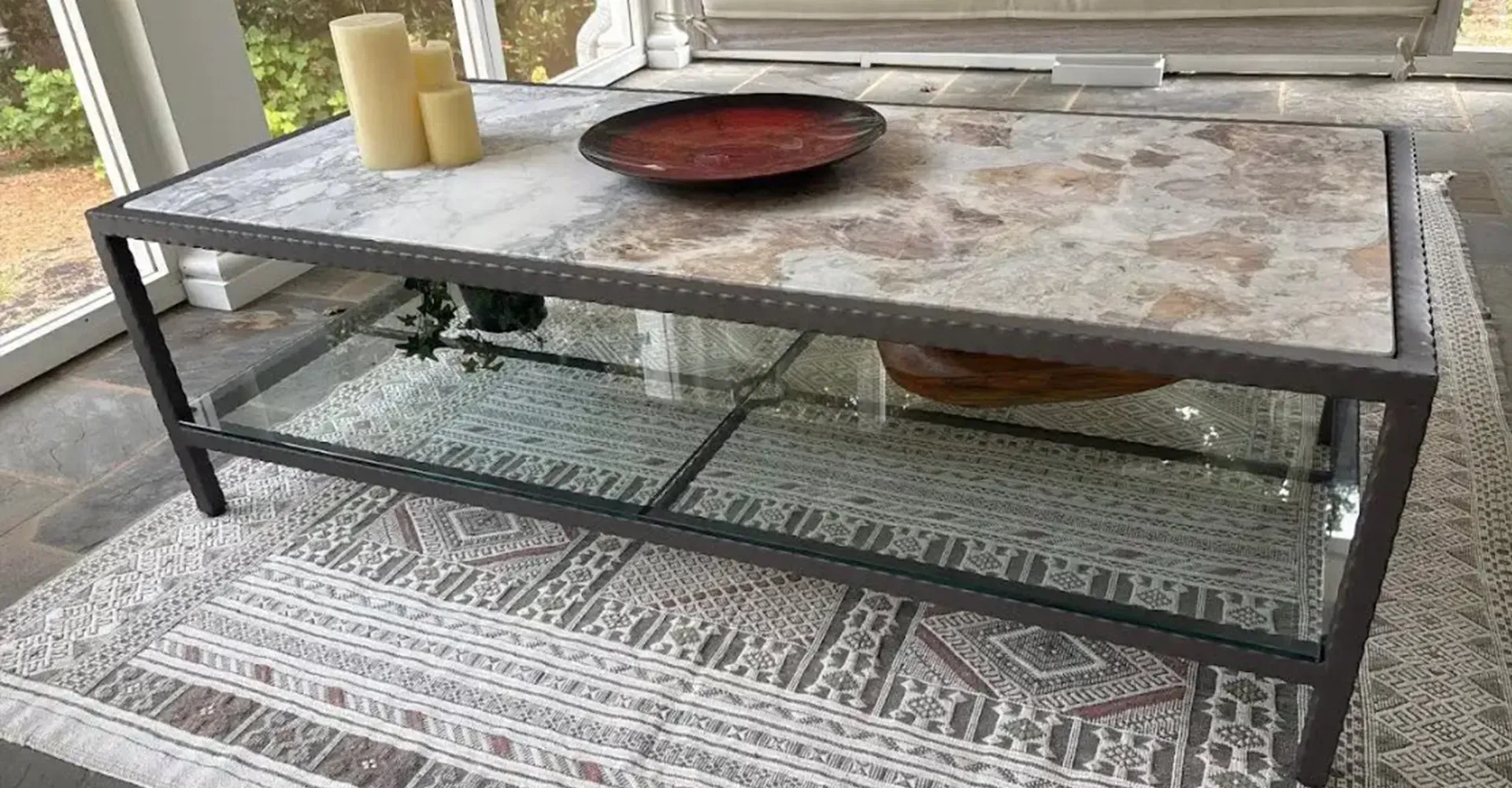 Outdoor patio coffee table with stone top, black metal frame, tray, candles, and decorative glass beneath